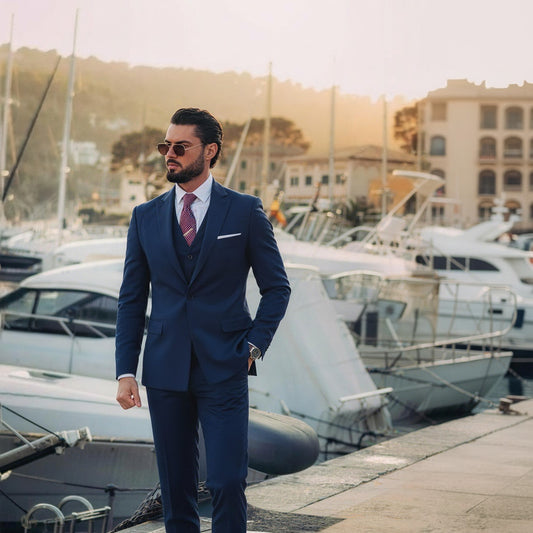 Navy # Men's slim fit 2-piece suit with peaked lapel and simple elegant design, navy formal blazer jacket with four-button cuffs and matching flat-front trousers with extended waist strap for business, office, wedding and daily wear, isolated on white background.